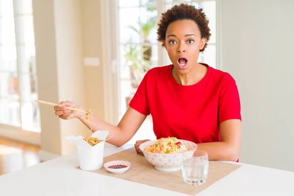 Young african american woman with afro hair eating asian food at home scared in shock with a surprise face, afraid and excited with fear expression