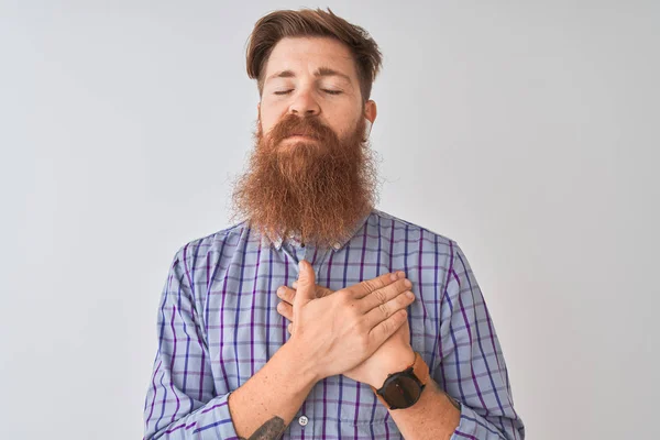 Redhead irish man listening to music using wireless earphones over isolated white background smiling with hands on chest with closed eyes and grateful gesture on face. Health concept.