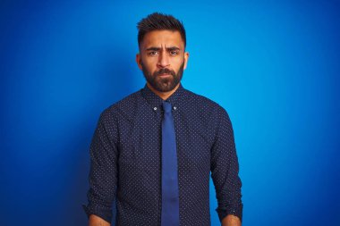 Genç Hint işadamı zarif gömlek ve kravat izole mavi arka plan üzerinde ayakta giyen ve sıkıntı için endişe, öfkeli ve korkuyor ağlıyor. Üzücü ifade.