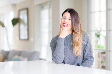 Evde kış kazak giyen genç güzel kadın emin çapraz kollar ve çeneme kaldırdı el ile gülümseme ile kameraya bakıyor. Pozitif düşünce.