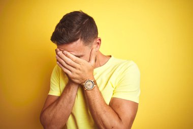 Ağlayan iken elleri ile yüz kapsayan üzücü ifade ile sarı izole arka plan üzerinde rahat sarı t-shirt giyen genç yakışıklı adam. Depresyon konsepti.
