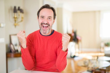 Yakışıklı orta yaş erkek evde geçirilen silahlarla şaşırmış ve başarı için hayran kutluyor ve gözleri açık. Kazanan kavramı.