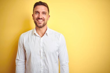 Yüz üzerinde mutlu ve serin bir gülümseme ile sarı izole arka plan üzerinde zarif beyaz gömlek giyen genç yakışıklı adam. Şanslı kişi.
