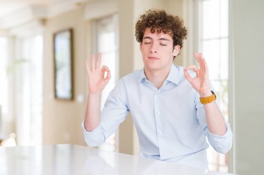 Kıvırcık okuma kafası ile genç iş adamı rahat ve gözler ile gülümseyen meditasyon jest parmaklar ile kapalı. Yoga konsepti.