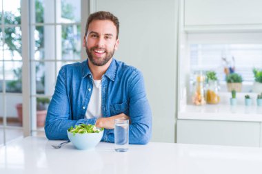 Yakışıklı adam yüz üzerinde mutlu ve serin bir gülümseme ile taze sağlıklı Salata yiyor. Şanslı kişi.