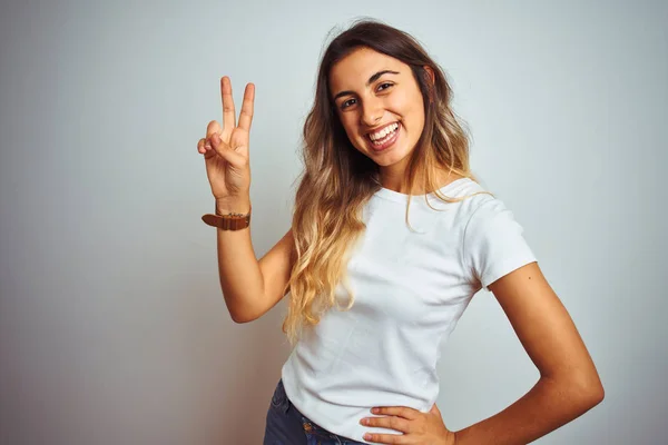 カジュアルな白いTシャツを着た若い美しい女性は 勝利のサインをしている指を示すカメラに微笑んで孤立した背景の上に ナンバー2 — ストック写真