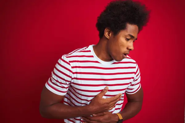 年轻的非洲裔美国男子穿着条纹T恤在孤立的红色背景与手在胃 因为恶心 疼痛的疾病感觉不适 疼痛概念 — 图库照片