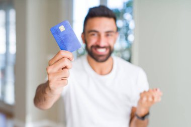 Yakışıklı İspanyol adam tutmak kredi kartı gurur çığlık ve kutlamak zafer ve başarı çok heyecanlı, tezahürat duygu