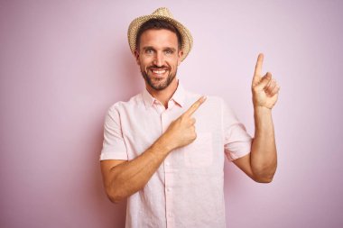 Pembe izole arka plan üzerinde şapka ve Yaz gömlek giyen yakışıklı adam gülümseyen ve yan iki el ve parmak ile işaret kamera bakıyor.