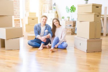 Evde karton kutular etrafında yerde oturan rahatlatıcı genç güzel çift, yeni bir eve hareket mutlu gülümseyen