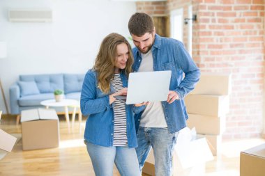 Yeni bir daireye taşımak için mutlu karton kutular etrafında bir odada bilgisayar laptop ayakta kullanarak genç çift