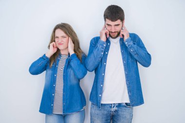 Beyaz izole arka plan üzerinde birlikte ayakta genç güzel çift yüksek sesle müzik gürültü için rahatsız ifade ile parmaklar ile kulakları kaplayan. Sağır kavramı.