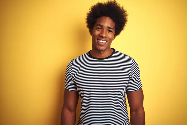 African american man with afro hair wearing navy striped t-shirt over isolated yellow background with a happy and cool smile on face. Lucky person.