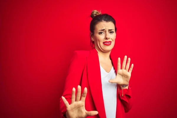 Young beautiful business woman standing over red isolated background disgusted expression, displeased and fearful doing disgust face because aversion reaction. With hands raised. Annoying concept.