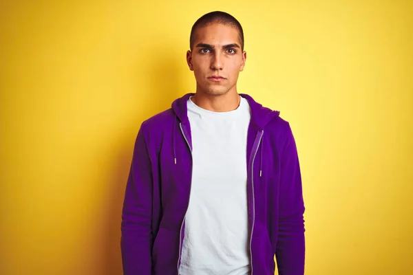 黄色の孤立した背景の上に紫色のスウェットシャツを着た若いハンサムな男は 顔に真剣な表情をしています カメラを見てシンプルで自然な — ストック写真