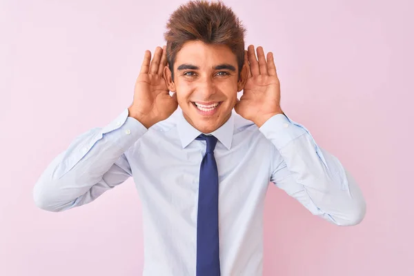 シャツとネクタイを着た若いハンサムなビジネスマンは 孤立したピンクの背景の上に立って 耳のジェスチャーに両手を聞こうとし ゴシップに興味を持っています 聴覚障害 聴覚障害 — ストック写真