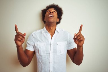 Afro saç ile Afrikalı Amerikan adam izole beyaz arka plan üzerinde ayakta gömlek giymiş şaşırdı ve bakıyor ve parmaklar ve yükseltilmiş kollar ile işaret şaşırttı.
