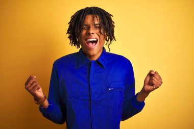 İzole sarı arka plan üzerinde mekanik üniforma giyen dreadlocks ile Afro işçi adam şaşırttı ve silah kaldırdı ve açık gözleri ile başarı için hayran kutluyor. Kazanan kavramı.