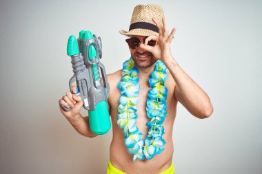 Genç adam yaz şapka giyiyor ve Hawaii Lei çiçek tutan göz parmaklarıyla görünümlü el ile ok işareti yapıyor gülümseyen mutlu yüz ile izole arka plan üzerinde su tabancası