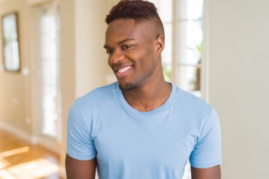 Rahat t-shirt giyen yakışıklı Afrikalı Amerikalı adam yüzüne gülümseme ile yan bakmak, doğal ifade. Güven gülüyor.