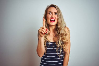 Beyaz izole arka plan üzerinde ayakta çizgili t-shirt giyen genç güzel kadın başarılı bir fikir parmak yukarı işaret. Çıkıldı ve mutlu. Bir numara.