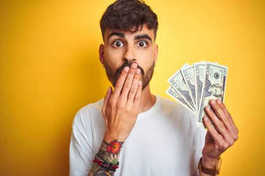 Dövme ile genç adam izole sarı arka plan kapağı ağız üzerinde ayakta el ile hata için utanç ile şok, korku ifade, sessizlik, gizli kavramı korkuyor