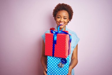 Afrika Amerikan kadın mutlu bir yüz ayakta ve kendine güvenen bir gülümseme dişleri gösteren ile gülümseyen pembe izole arka plan üzerinde Doğum günü hediyeleri tutarak