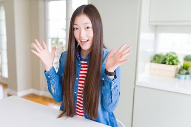 Güzel Asyalı kadın giyiyor denim beyaz masa kutluyor saçma sapan şeylerden ceket ve başarı için kaldırdı Kollarını açarak hayret ve heyecanlı çığlık gözleri açık. Kazanan kavramı