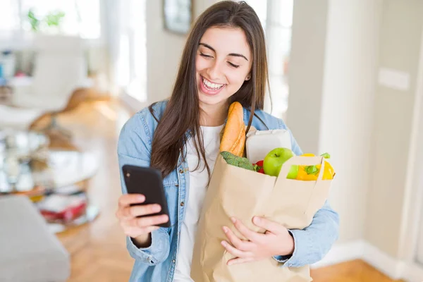 Молода Жінка Тримає Паперовий Мішок Повний Свіжих Продуктів Використовує Додаток — стокове фото