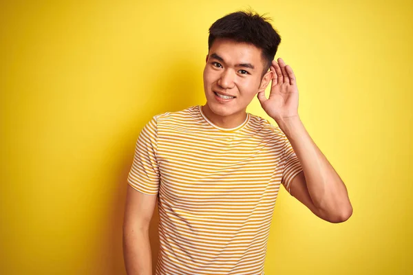孤立した黄色の背景の上に立つTシャツを着たアジアの若い中国人男性は 噂やゴシップに耳を傾けて耳をつんじんで微笑んでいる 聴覚障害の概念 — ストック写真