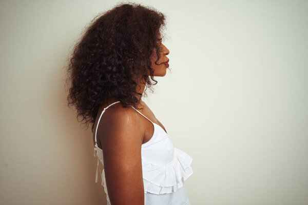 Young african american woman wearing t-shirt standing over isolated white background looking to side, relax profile pose with natural face with confident smile.