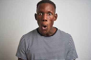 Izole beyaz arka plan üzerinde duran lacivert çizgili t-shirt giyen Afro-Amerikan adam sürpriz bir yüz ile şok korkmuş, korku ifade korku ve heyecanlı