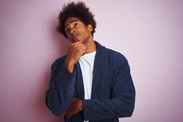 Young african american man wearing pajama standing over isolated pink background with hand on chin thinking about question, pensive expression. Smiling with thoughtful face. Doubt concept.