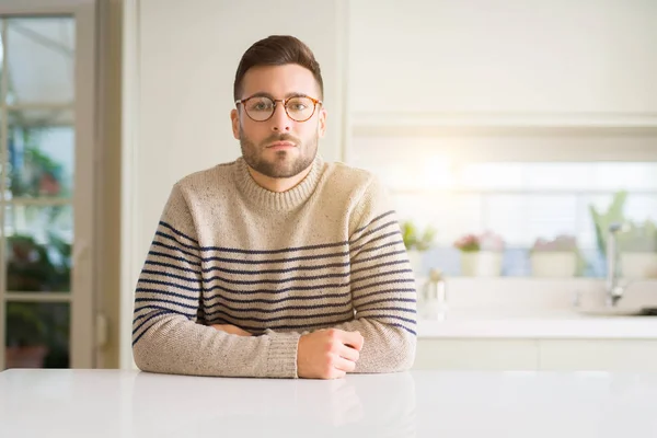 Young handsome man wearing glasses at home with serious expression on face. Simple and natural looking at the camera.