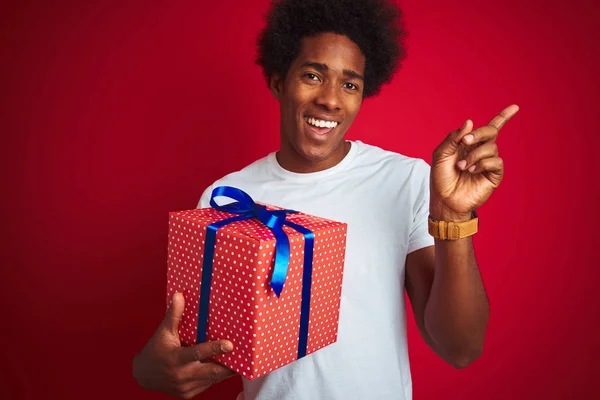 Joven Afroamericano Hombre Sosteniendo Regalo Cumpleaños Pie Sobre Fondo Rojo —  Fotos de Stock