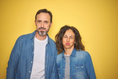 Güzel orta yaş çift birlikte komik yüz ile izole sarı arka plan PU, yanakları üzerinde denim gömlek giyiyor. Ağız hava ile şişirilmiş, çılgın ifade.