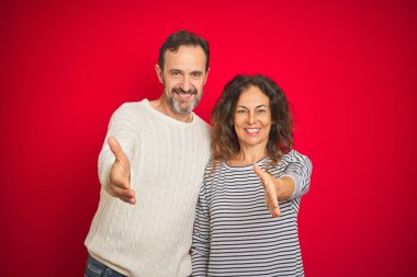 Güzel orta yaş çift izole kırmızı arka plan üzerinde kış kazak giyen dostça tebrik ve karşılama olarak el sıkışması sunuyor. Başarılı iş.