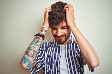 Dövme ile genç adam izole beyaz arka plan üzerinde duran çizgili gömlek ayakta baş ağrısı umutsuz ve vurguladı çünkü ağrı ve migren. Eller baş.