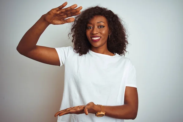 Young african american woman wearing t-shirt standing over isolated white background gesturing with hands showing big and large size sign, measure symbol. Smiling looking at the camera. Measuring concept.