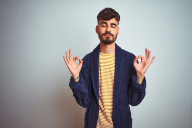 İzole beyaz arka plan üzerinde ayakta bornoz giymiş dövme ile genç adam Relax ve gözleri ile gülümseyen meditasyon jest parmaklar ile kapalı. Yoga konsepti.