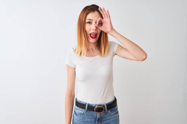 Güzel kızıl saçlı kadın rahat t-shirt üzerinde ayakta giyen izole beyaz arka plan ile ok jest yapıyor el gülümseyen, göz görünümlü parmaklar ile mutlu yüz.