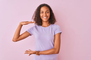 Genç Brezilyalı kadın, büyük ve büyük boyutlu işareti, ölçmek sembolü gösteren eller ile izole pembe arka plan üzerinde ayakta t-shirt giymiş. Kameraya bakarak gülümsüyor. Ölçme konsepti.