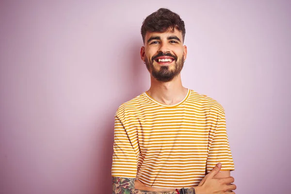 黄色い縞模様のTシャツを着た若い男は カメラを見て腕を組んで微笑む孤立したピンクの背景の上に立っています ポジティブな人 — ストック写真