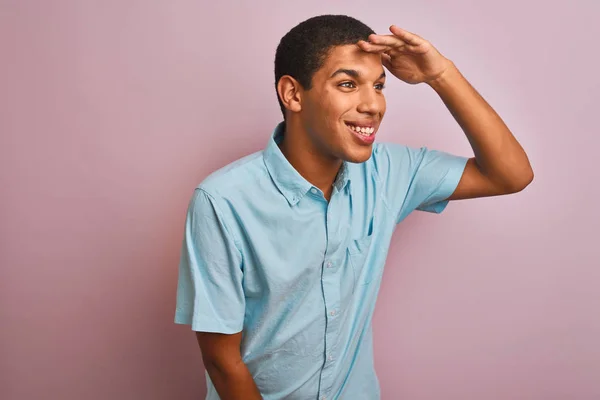 年轻的英俊阿拉伯男子穿着蓝色衬衫站在孤立的粉红色背景很高兴和微笑看着远方的手在头上 搜索概念 — 图库照片