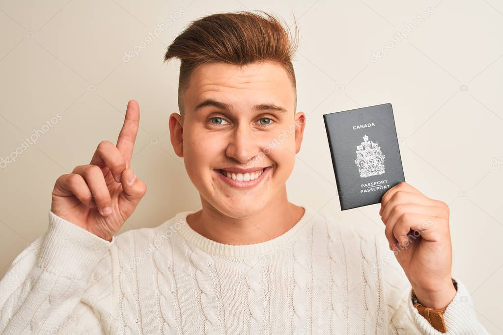 Young handsome man holding Canada Canadian passport over isolated white background surprised with an idea or question pointing finger with happy face, number one