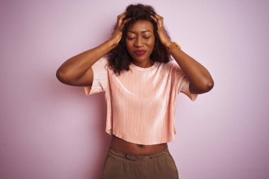 Genç afro-amerikan kadın izole pembe arka plan üzerinde ayakta t-shirt giyen baş ağrısı umutsuz muzdarip ve stresli çünkü ağrı ve migren. Eller baş üstünde.