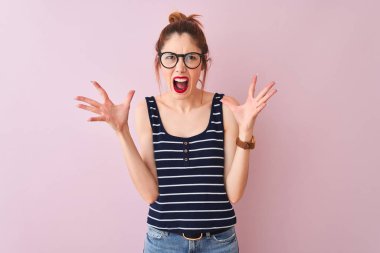 Çizgili t-shirt izole pembe arka plan çılgın ve deli çığlık ve agresif ifade ve kollar ile bağırarak üzerine ayakta giyen Pigtail ile Redhead kadın kaldırdı. Hayal kırıklığı kavramı.