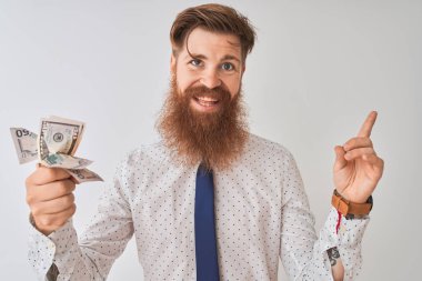 Genç Redhead İrlandalı işadamı tutan dolar izole beyaz arka planda ayakta çok mutlu yan el ve parmak ile işaret