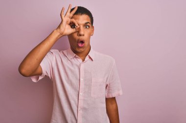 İzole pembe arka plan üzerinde duran rahat gömlek giyen genç yakışıklı Arap adam ok jest yaparak şaşırmış yüz ile şok, parmaklardan bakarak göz. İnanmayan ifade.