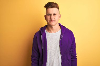 Mor sweatshirt giyen genç yakışıklı adam izole sarı arka plan üzerinde duran yan bakarak ve düşünme uzak bakıyor.